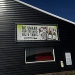 Banner on a dark corrugated exterior promoting Zeeland flavors at home, featuring wine bottles and gift boxes.